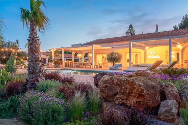 Die Villa am Abend: beleuchtete Terrasse, Pool und Garten mit Palmen.